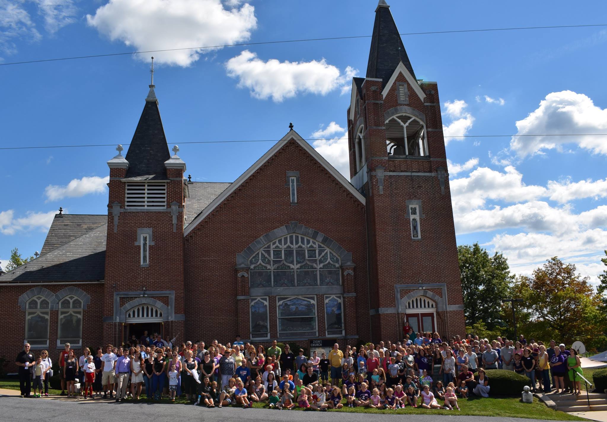large crowd of all ages posing outside the front of zions church on a sunny day