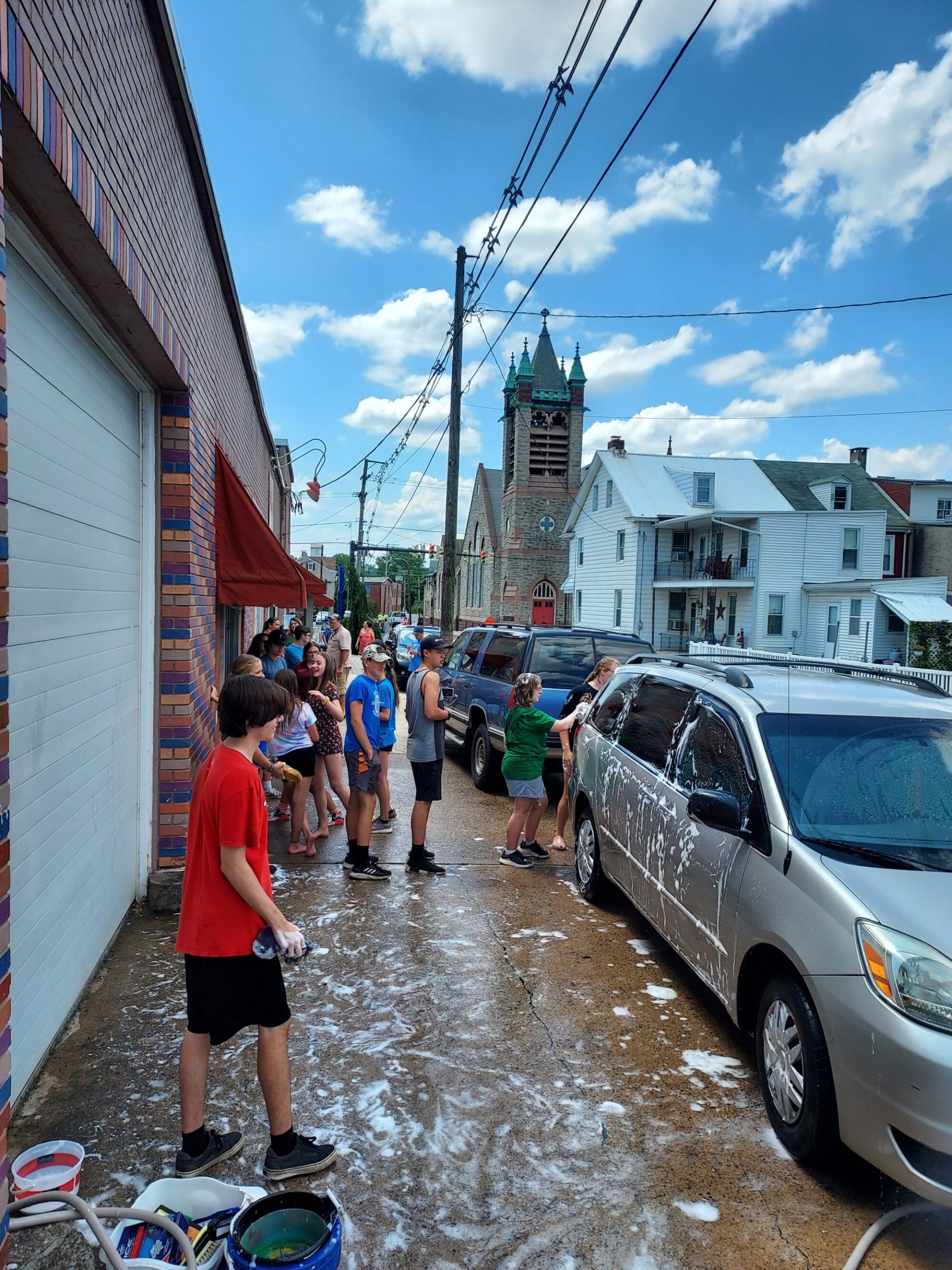 several teens standing on a sidewalk with car washing supplies